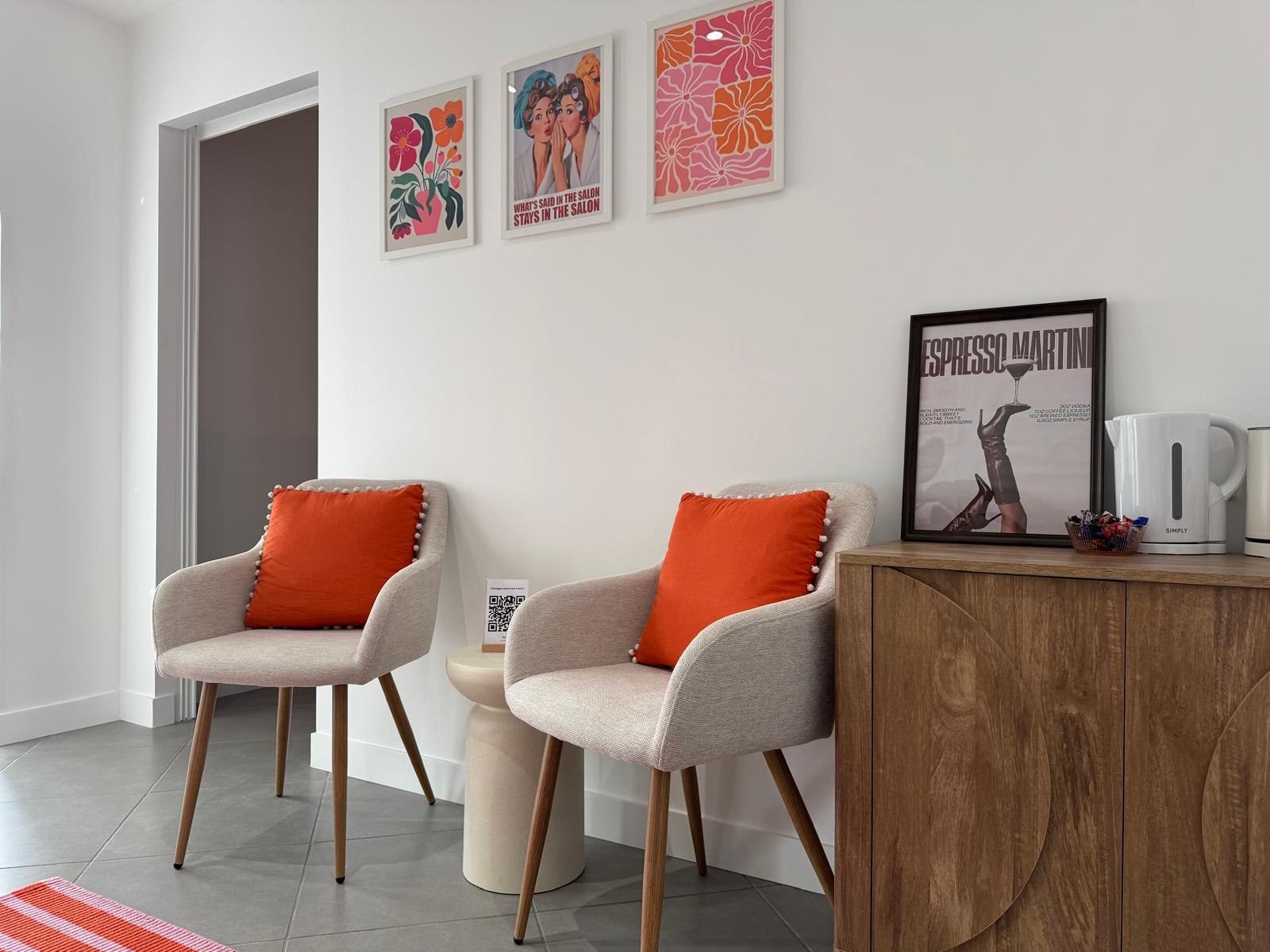 Espace d'accueil : deux fauteuils beiges à coussins orange, affiches colorées au mur et meuble en bois.